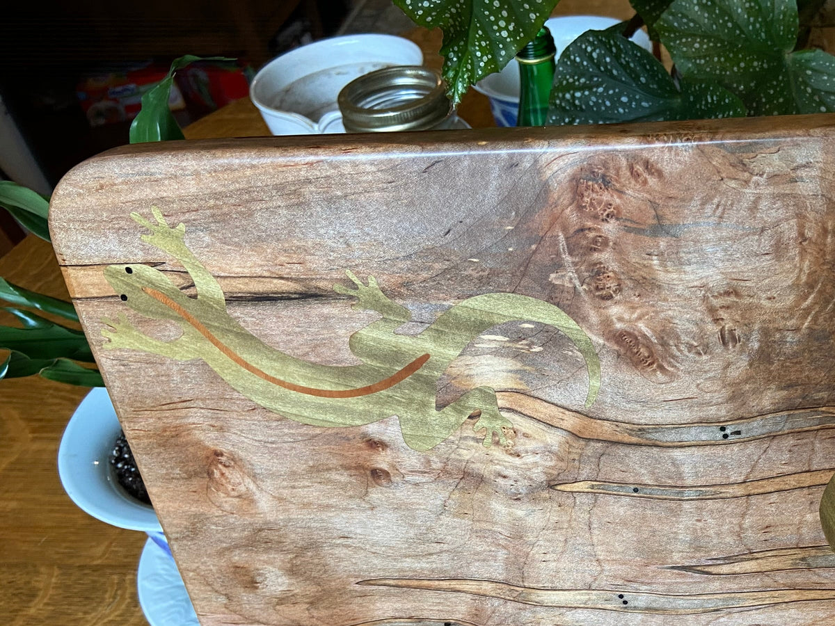 Wooden cutting board with a stand on a wooden surface, surrounded by plants.